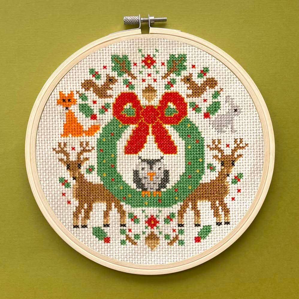 Cross-stitched wreath with animals in an embroidery hoop on a green background