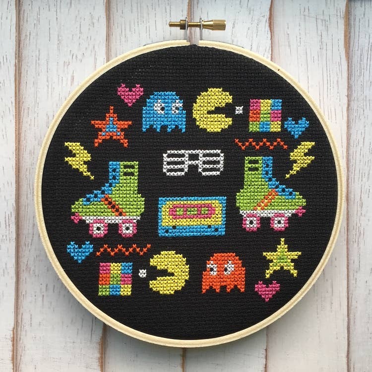 Cross-stitched design of retro-themed characters and symbols in a wooden hoop.